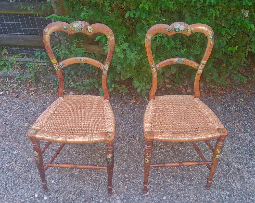 A pair of Victorian side chairs featuring light brown wooden frames adorned with hand-painted floral motifs and woven cane seats. View X