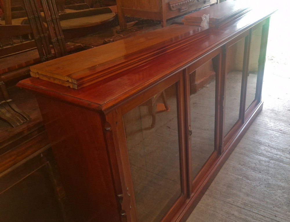 A large late Victorian mahogany low bookcase featuring four glazed glass doors with removable timber shelves resting in front. View V