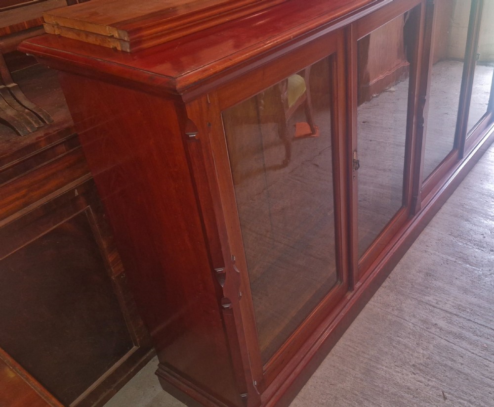 A large late Victorian mahogany low bookcase featuring four glazed glass doors with removable timber shelves resting in front. View IX