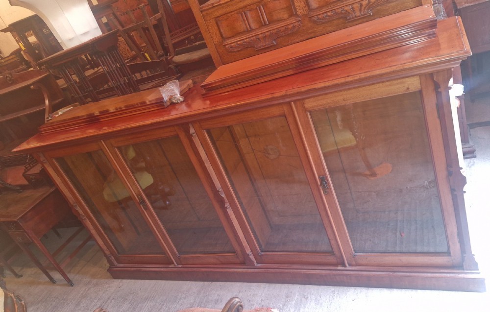 A large late Victorian mahogany low bookcase featuring four glazed glass doors with removable timber shelves resting in front. View XX