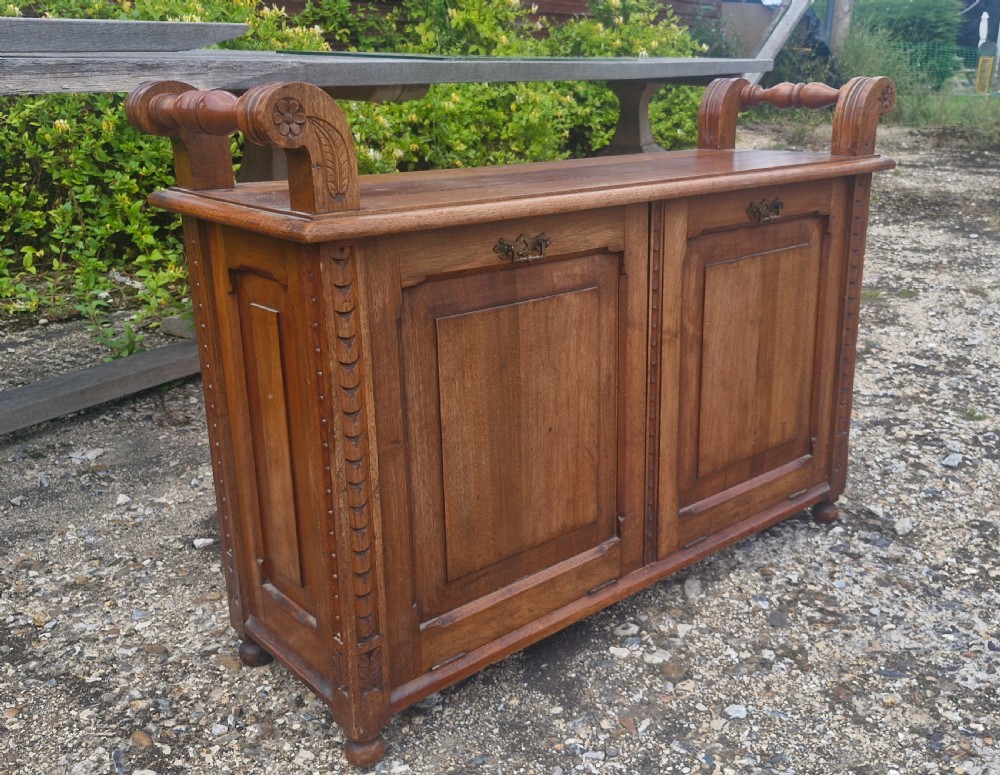 A late Victorian carved oak duet stool with two panelled cabinet doors, brass drop handles, and raised side scroll handles.