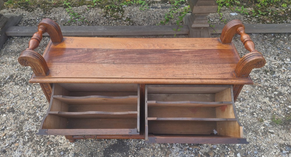 A late Victorian carved oak duet stool with two panelled cabinet doors, brass drop handles, and raised side scroll handles. View II