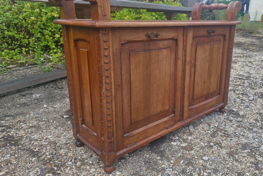 A late Victorian carved oak duet stool with two panelled cabinet doors, brass drop handles, and raised side scroll handles. View V