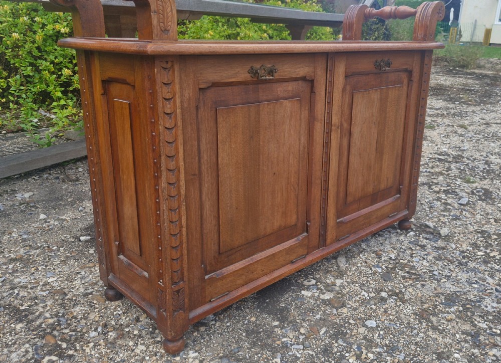 A late Victorian carved oak duet stool with two panelled cabinet doors, brass drop handles, and raised side scroll handles. View VI