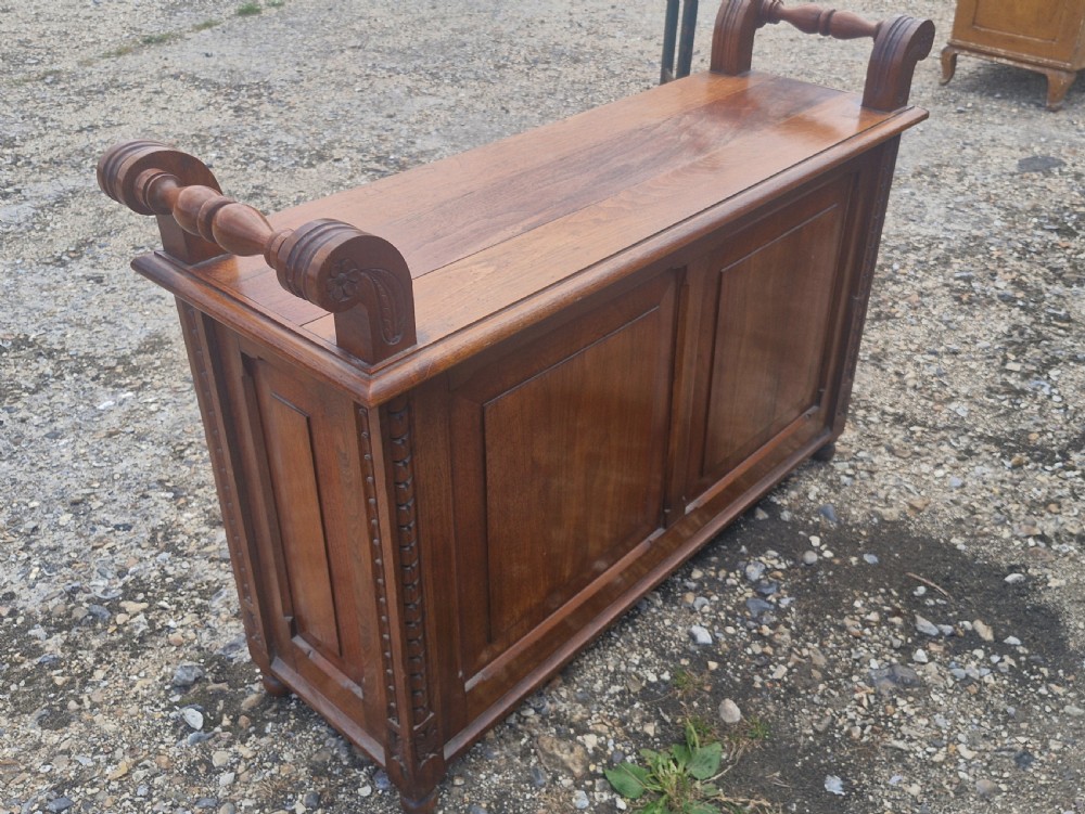 A late Victorian carved oak duet stool with two panelled cabinet doors, brass drop handles, and raised side scroll handles. View VII