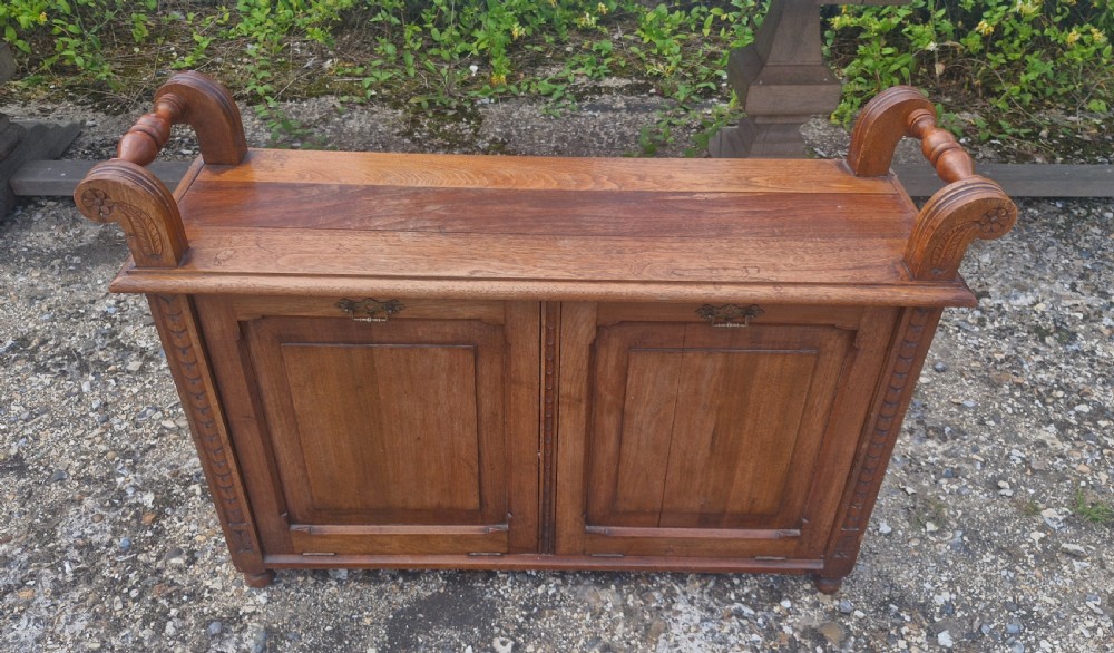 A late Victorian carved oak duet stool with two panelled cabinet doors, brass drop handles, and raised side scroll handles. View VIII