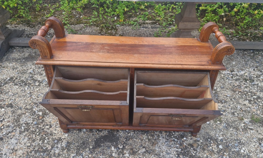 A late Victorian carved oak duet stool with two panelled cabinet doors, brass drop handles, and raised side scroll handles. View XI