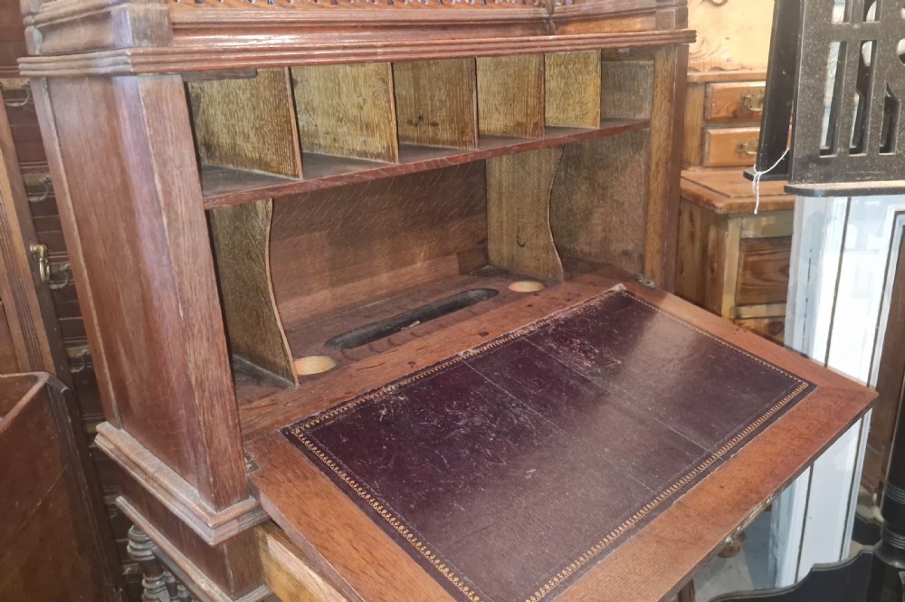 A late Victorian dark oak writing bureau featuring a pierced carved top gallery, fall-front drop lid with brass hardware, and a lower tambour door compartment. View XI