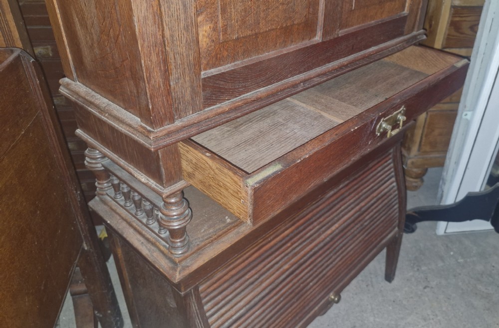 A late Victorian dark oak writing bureau featuring a pierced carved top gallery, fall-front drop lid with brass hardware, and a lower tambour door compartment. View XII