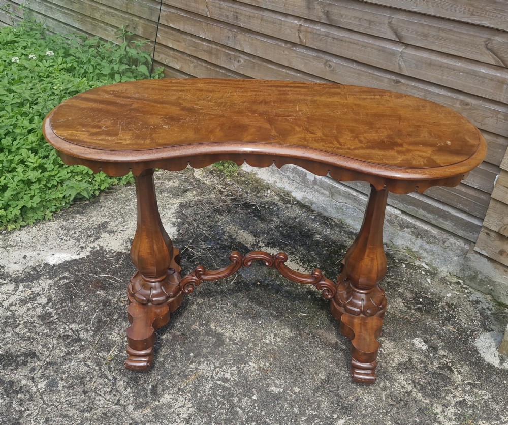 A mid-19th-century mahogany kidney-shaped side table featuring turned pedestal supports, a carved scrolled stretcher, and shaped feet.
