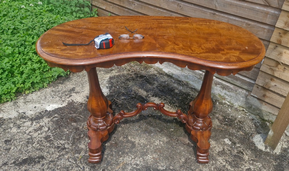 A mid-19th-century mahogany kidney-shaped side table featuring turned pedestal supports, a carved scrolled stretcher, and shaped feet. View X