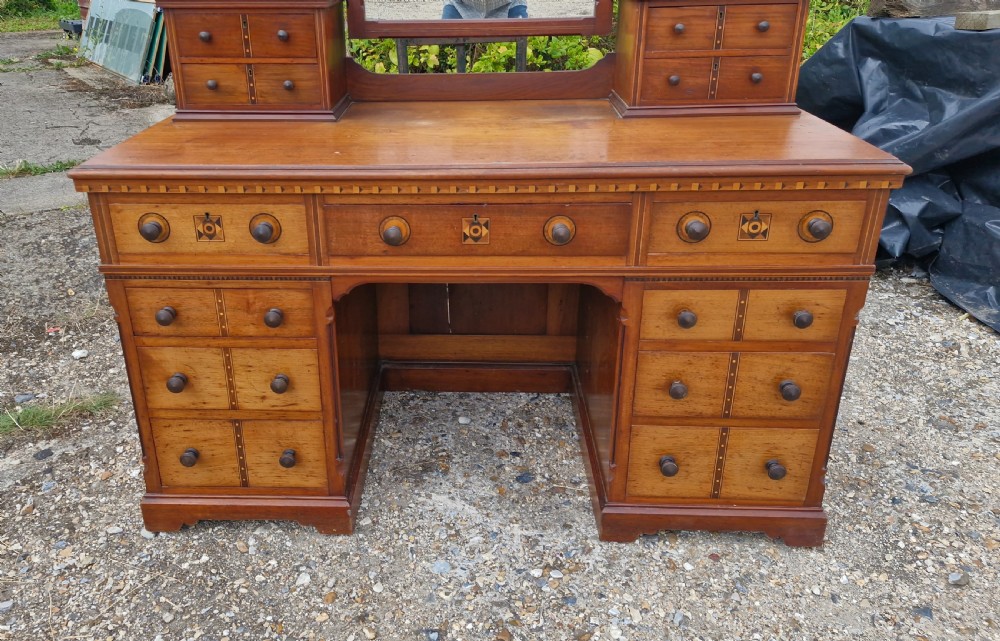 A late Victorian Aesthetic Movement wooden kneehole dressing table featuring geometric inlay, multiple drawers with knob handles, and a central rectangular mirror flanked by trinket drawers. View VI