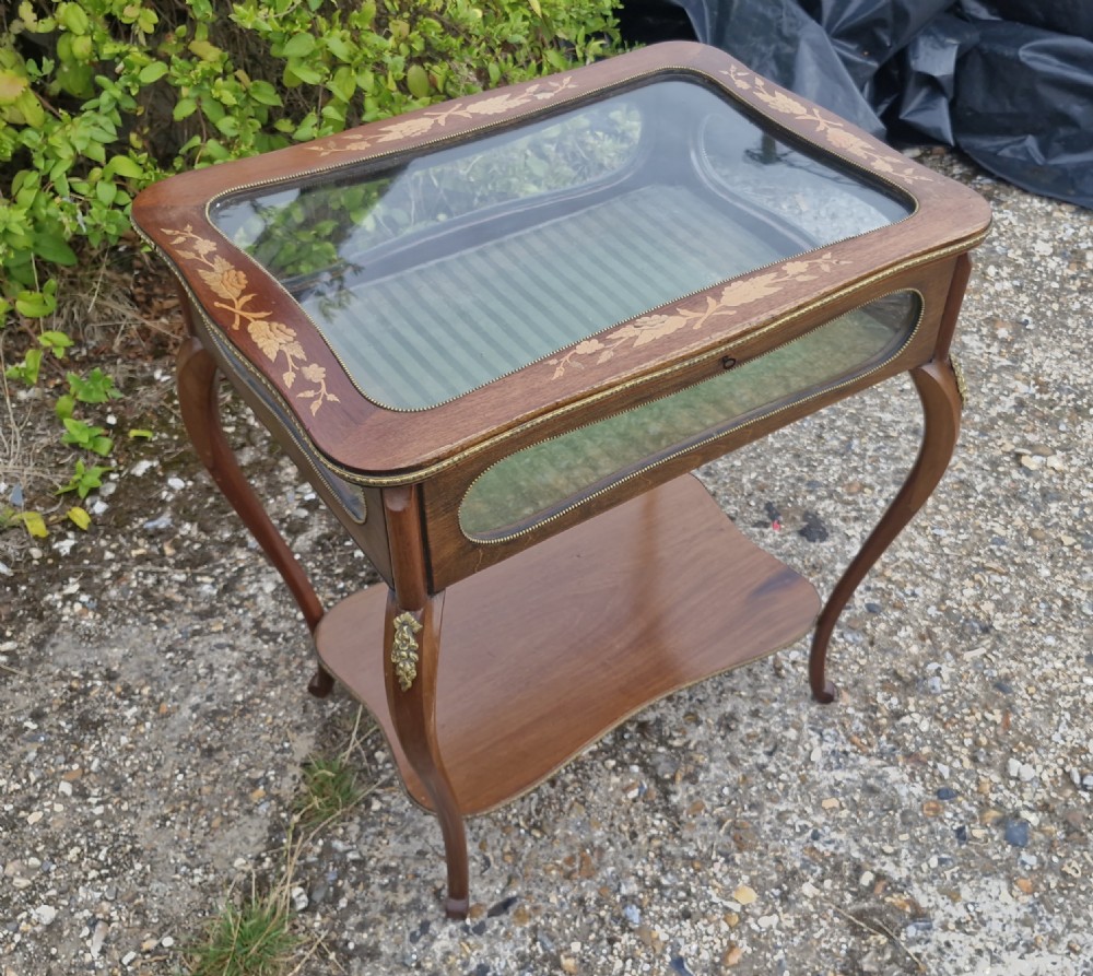 An Edwardian mahogany bijouterie table featuring floral marquetry inlay on the hinged glass top, slender cabriole legs, brass mounts, and a green fabric-lined interior. View VI