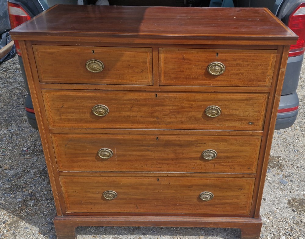 An Edwardian mahogany chest of drawers with linear string inlay borders, two short top drawers, three long lower drawers, and brass oval swing handles.