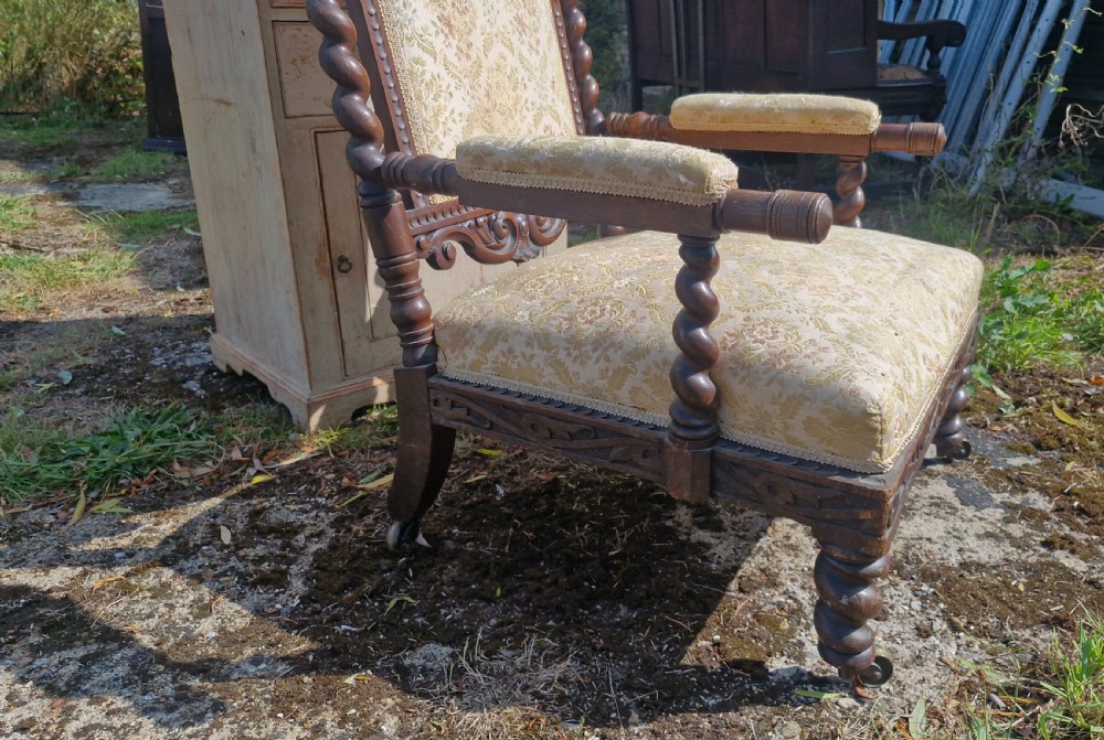 A mid-Victorian carved oak open armchair featuring barley twist supports, an ornate carved cresting rail, beige damask fabric upholstery, and brass castors. View X