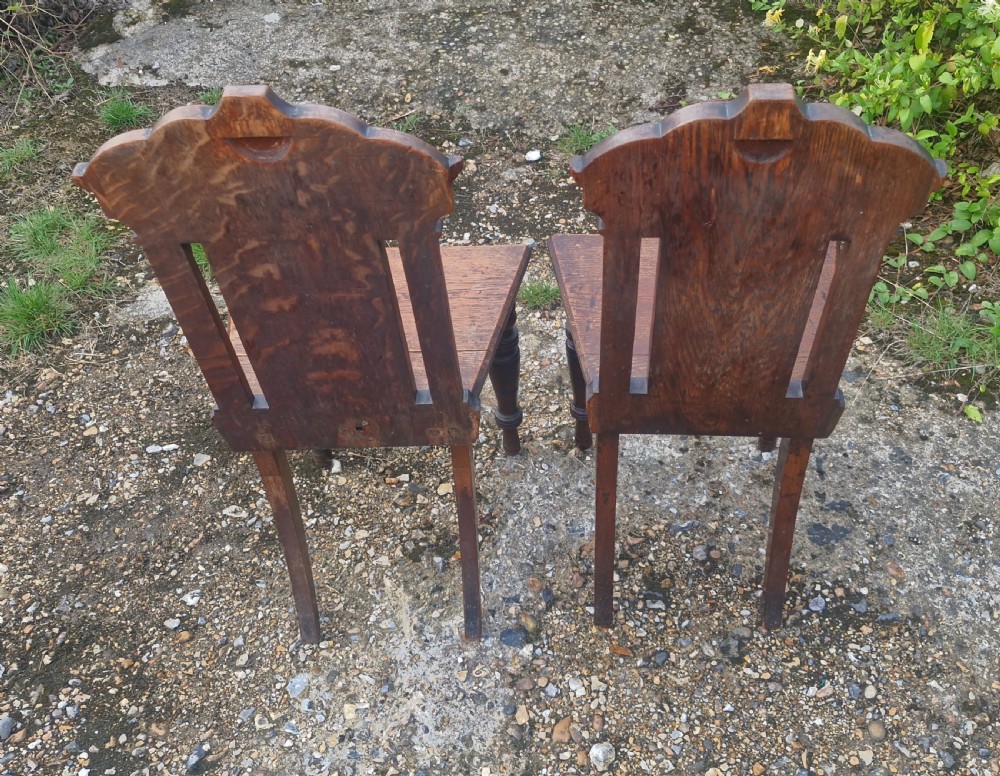 A pair of dark oak hall chairs featuring inset ceramic tiles with historic figures in the backrests, solid seats, and turned front legs. View V