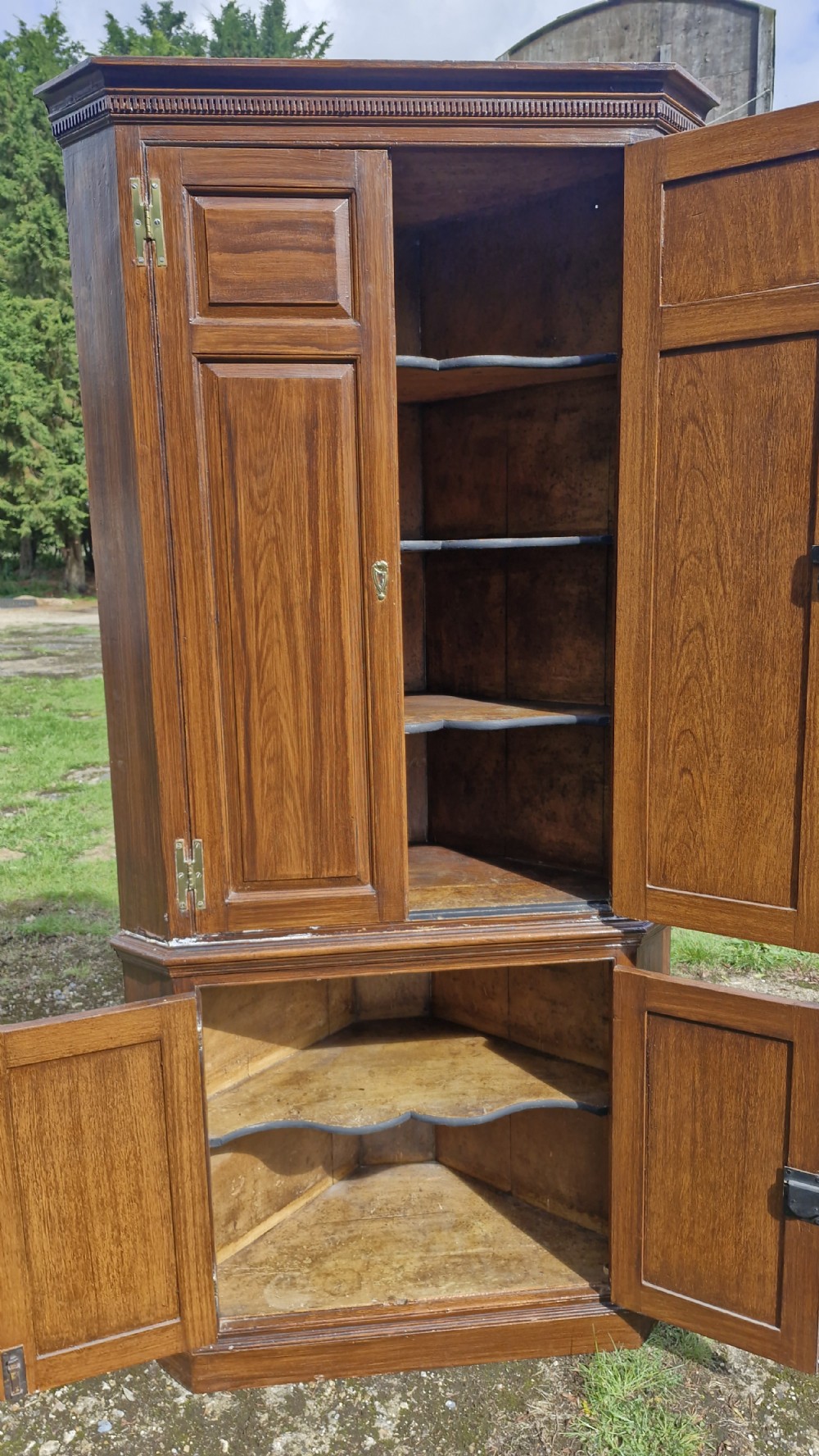 A late Georgian two-part pine corner cupboard featuring a scumble-glazed simulated oak grain finish, panelled doors, dentil moulding along the top cornice, and brass hardware.