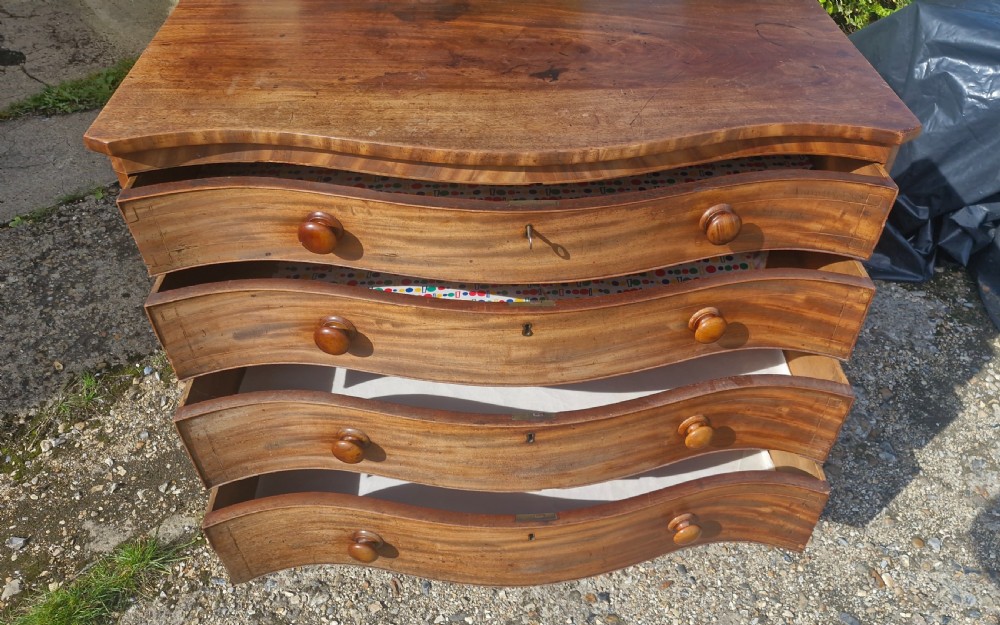 An early 19th-century mahogany serpentine chest of drawers featuring four graduated drawers with turned wooden knobs and a contoured front. View VII