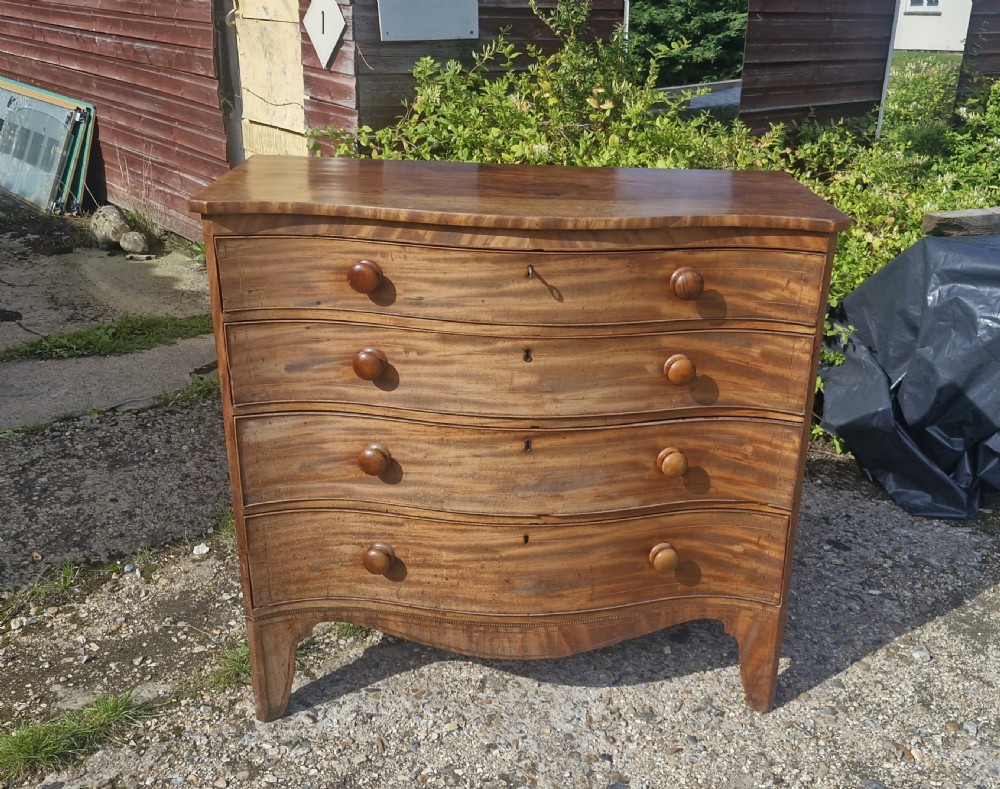 An early 19th-century mahogany serpentine chest of drawers featuring four graduated drawers with turned wooden knobs and a contoured front. View IX