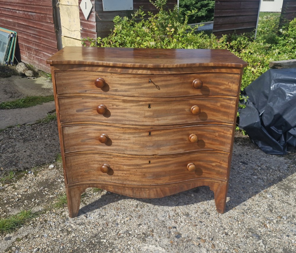 An early 19th-century mahogany serpentine chest of drawers featuring four graduated drawers with turned wooden knobs and a contoured front. View X