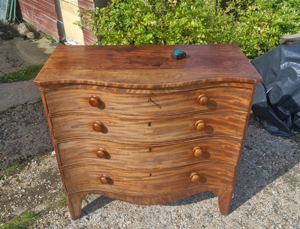 An early 19th-century mahogany serpentine chest of drawers featuring four graduated drawers with turned wooden knobs and a contoured front. View XI