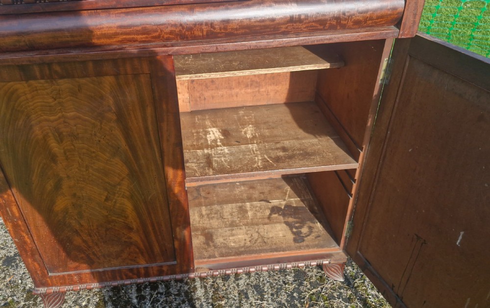 A Regency mahogany two-door side cabinet featuring a raised shelf with turned posts, carved cresting, and panelled flame mahogany doors. View V
