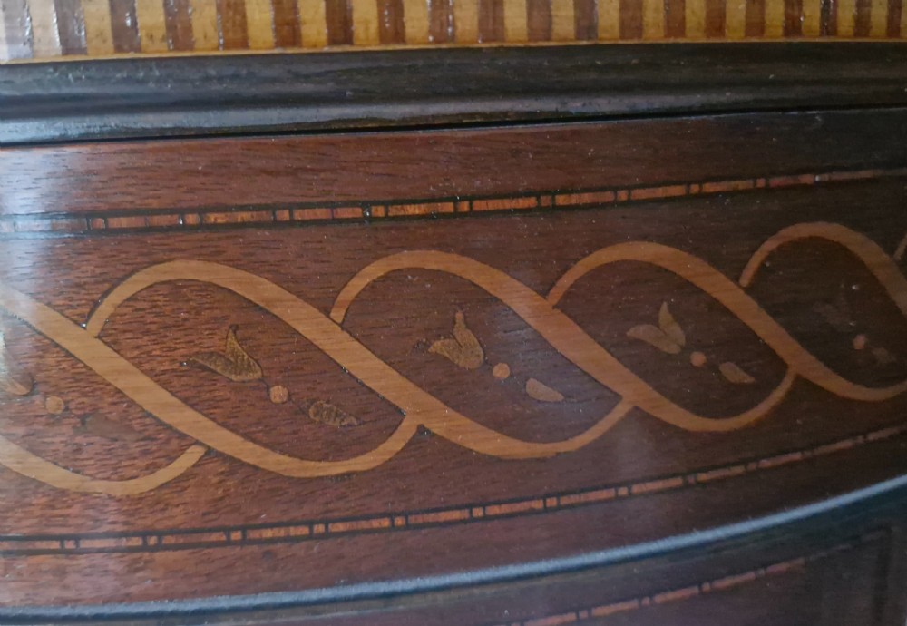An Edwardian demi-lune mahogany display cabinet with curved glass sides, inlaid decorative banding along the top, and light interior shelves raised on slender legs. View III