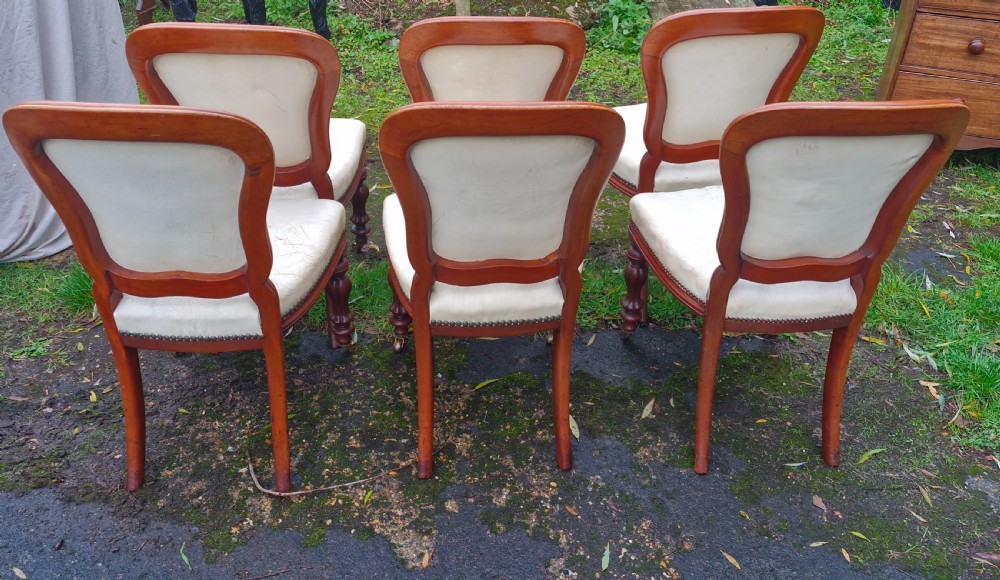A set of six mid-Victorian mahogany dining chairs with cream upholstered balloon backs, brass studding, and turned front legs on castors. View VII