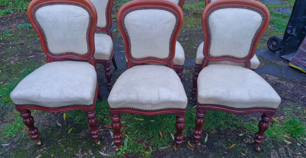 A set of six mid-Victorian mahogany dining chairs with cream upholstered balloon backs, brass studding, and turned front legs on castors. View IX