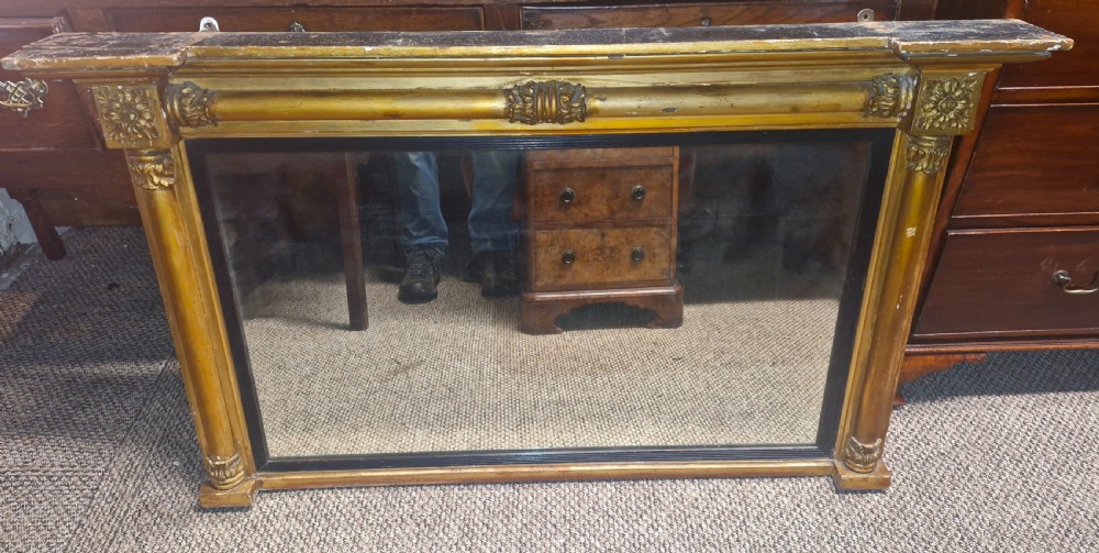 A 19th-century rectangular giltwood overmantel mirror featuring side pilasters, rosette corner mounts, and an ebonised inner slip.