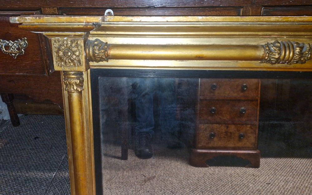 A 19th-century rectangular giltwood overmantel mirror featuring side pilasters, rosette corner mounts, and an ebonised inner slip. View IV
