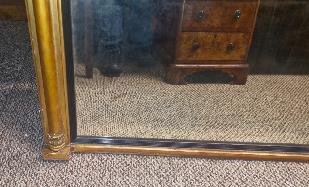 A 19th-century rectangular giltwood overmantel mirror featuring side pilasters, rosette corner mounts, and an ebonised inner slip. View V