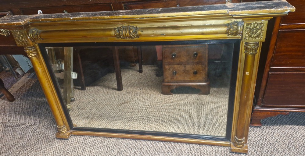 A 19th-century rectangular giltwood overmantel mirror featuring side pilasters, rosette corner mounts, and an ebonised inner slip. View VI