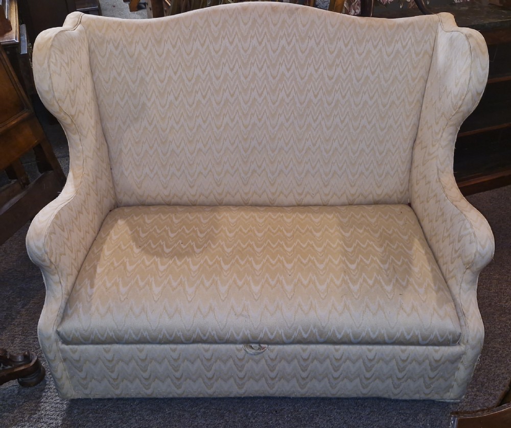 A high-backed two-seater wingback sofa upholstered in cream chevron patterned fabric with an enclosed storage box base.