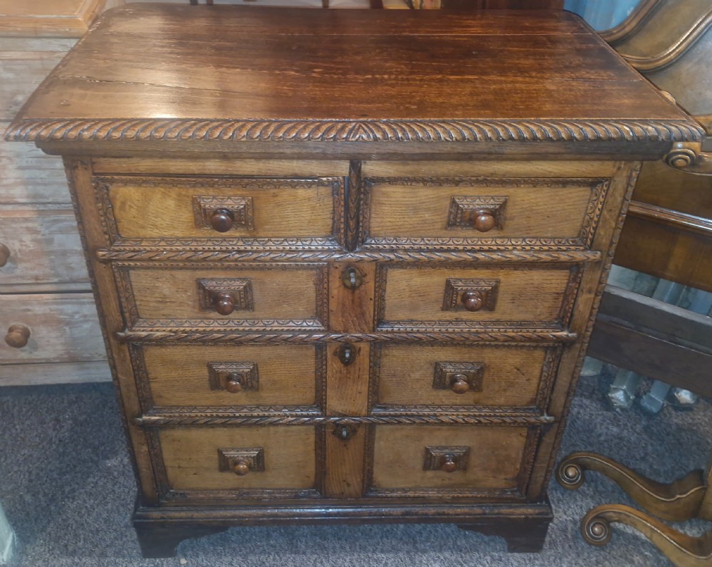 An early eighteenth-century dark oak chest of drawers featuring carved mouldings and wooden turned knobs.