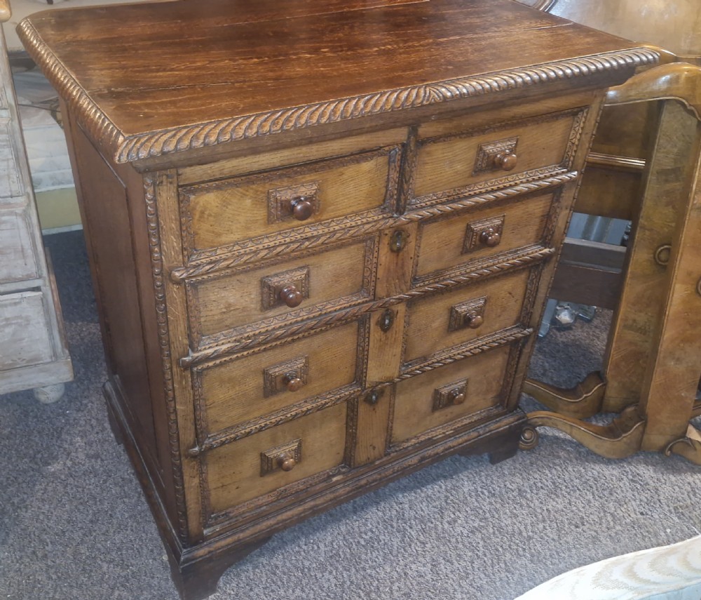 An early eighteenth-century dark oak chest of drawers featuring carved mouldings and wooden turned knobs. View II