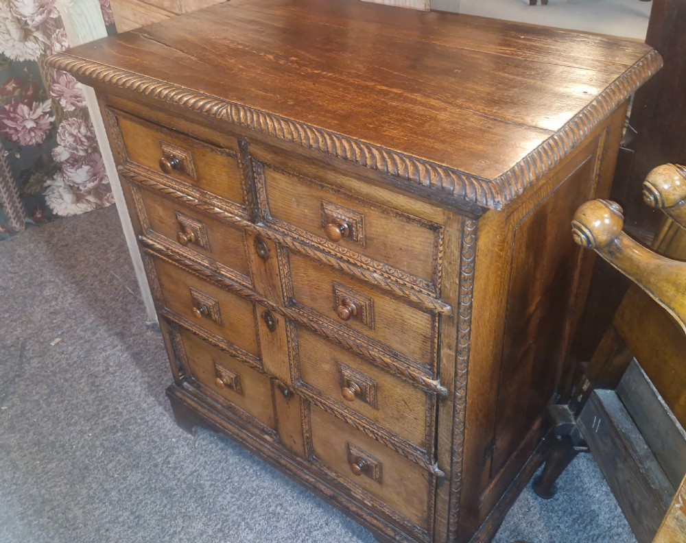 An early eighteenth-century dark oak chest of drawers featuring carved mouldings and wooden turned knobs. View III