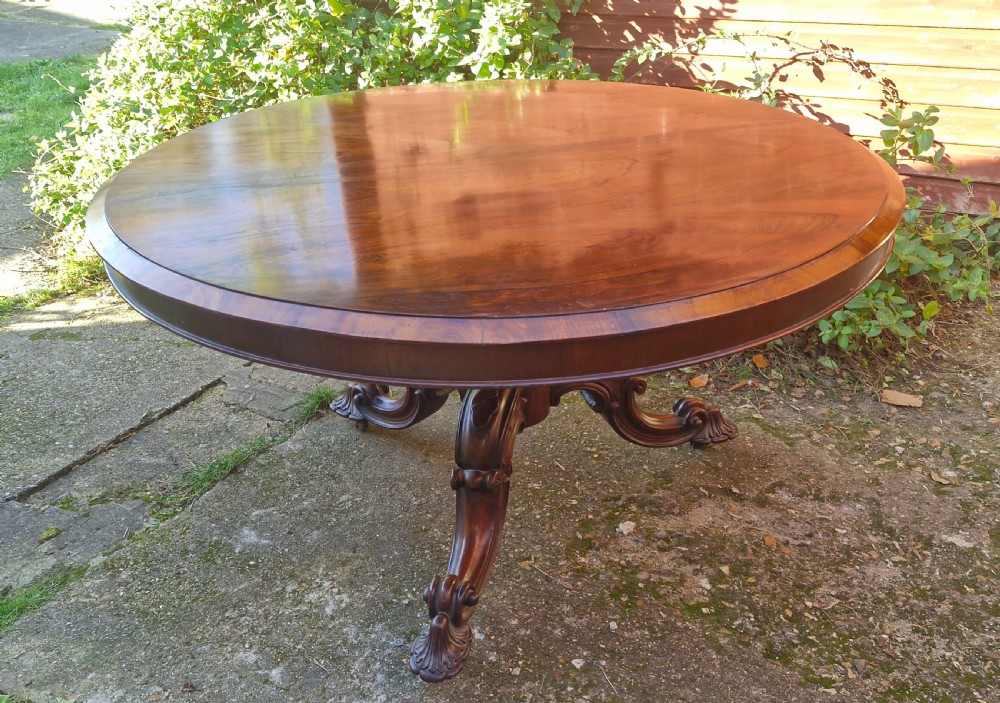 A circular mid-19th-century rosewood centre table featuring a polished top, deep apron, and ornate carved pedestal legs.