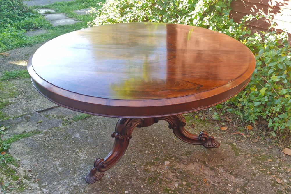 A circular mid-19th-century rosewood centre table featuring a polished top, deep apron, and ornate carved pedestal legs. View VI