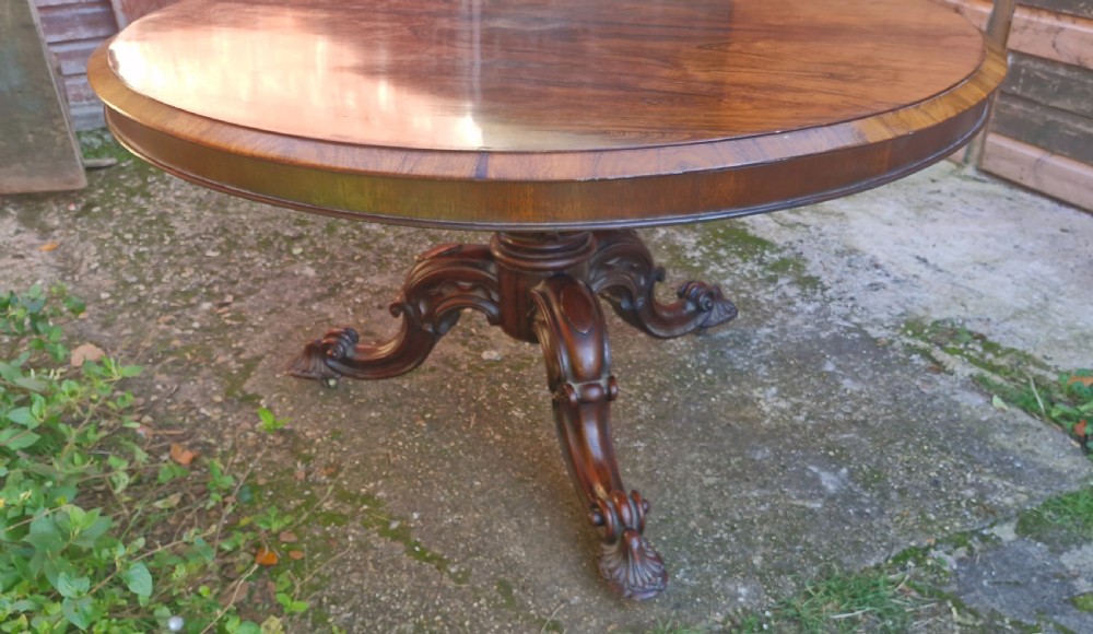 A circular mid-19th-century rosewood centre table featuring a polished top, deep apron, and ornate carved pedestal legs. View VIII