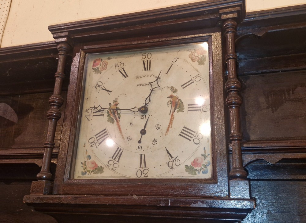 A nineteenth-century dark oak clock dresser featuring an integrated central clock dial, open display shelves, small drawers, and a lower cabinet structure with brass handles. View VII