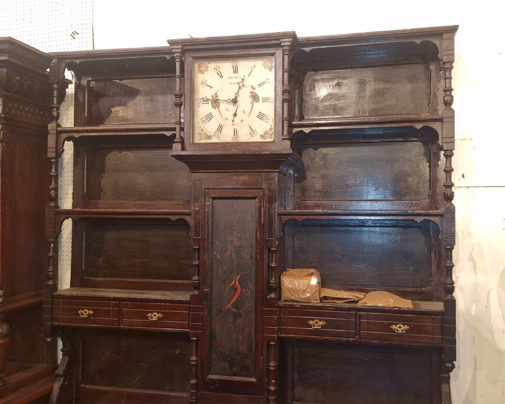 A nineteenth-century dark oak clock dresser featuring an integrated central clock dial, open display shelves, small drawers, and a lower cabinet structure with brass handles. View VIII