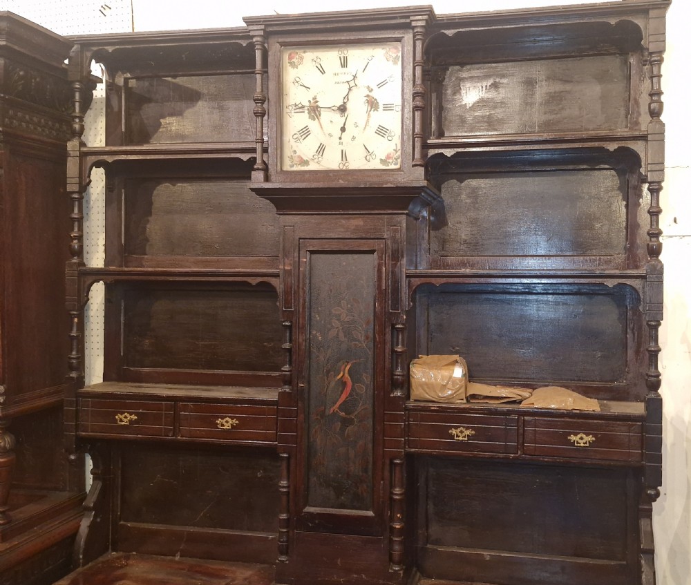 A nineteenth-century dark oak clock dresser featuring an integrated central clock dial, open display shelves, small drawers, and a lower cabinet structure with brass handles. View IX