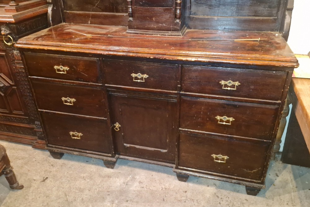 A nineteenth-century dark oak clock dresser featuring an integrated central clock dial, open display shelves, small drawers, and a lower cabinet structure with brass handles. View X