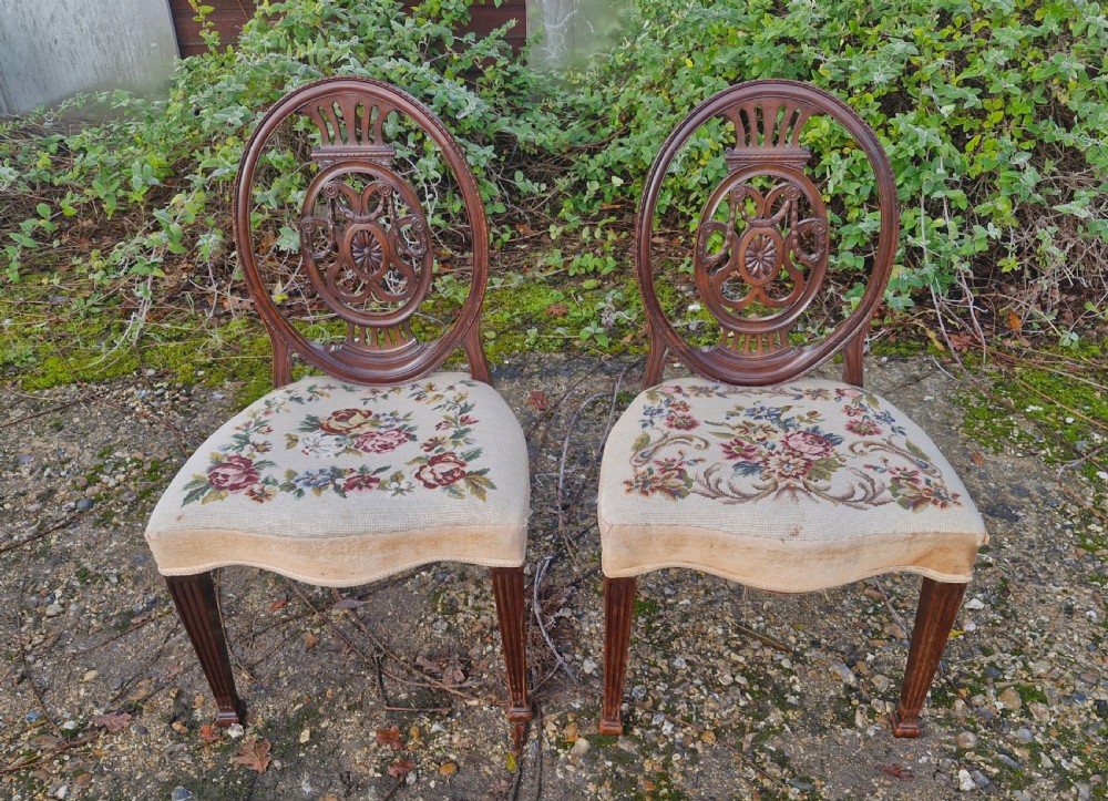 A pair of early 19th-century mahogany side chairs featuring carved oval splats and floral needlepoint upholstered seats.