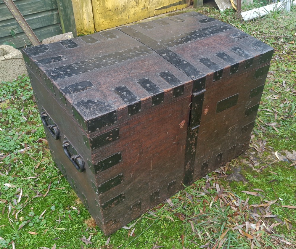 A mid-19th century dark oak silver chest featuring heavy iron corner straps, metal banding, split lid design, and side handles.