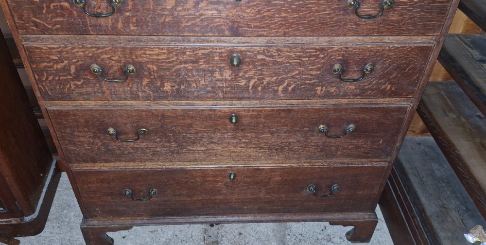 A Georgian oak chest of drawers featuring two short drawers over four long graduating drawers with brass swan-neck handles and bracket feet. View III