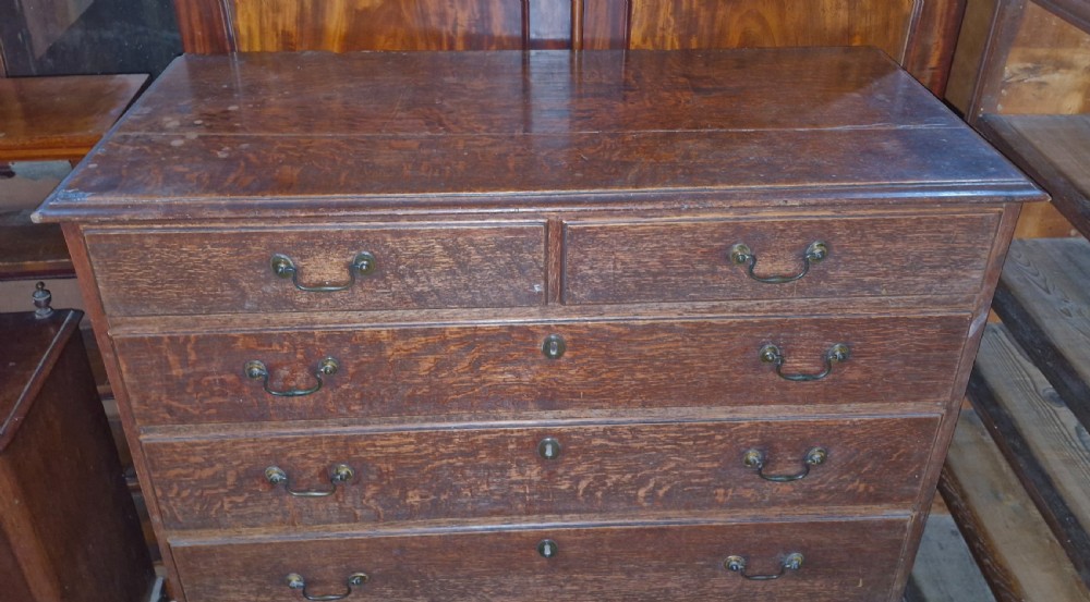 A Georgian oak chest of drawers featuring two short drawers over four long graduating drawers with brass swan-neck handles and bracket feet. View VII