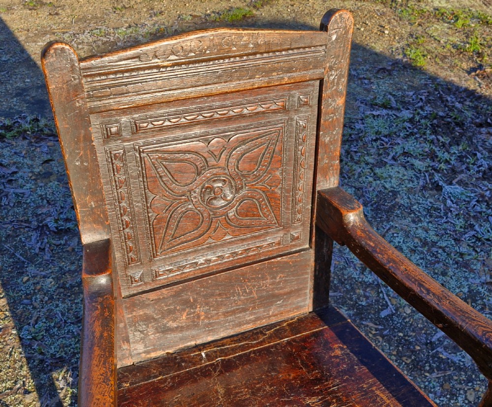 A dark carved oak childs wainscot armchair featuring a carved floral back panel, shaped armrests, and decorative carved seat rail. View II