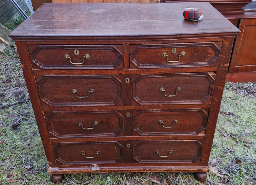 An 18th-century dark oak chest of drawers featuring geometric octagonal panel mouldings, brass drop handles, keyhole escutcheons, and turned bun feet. View VIII
